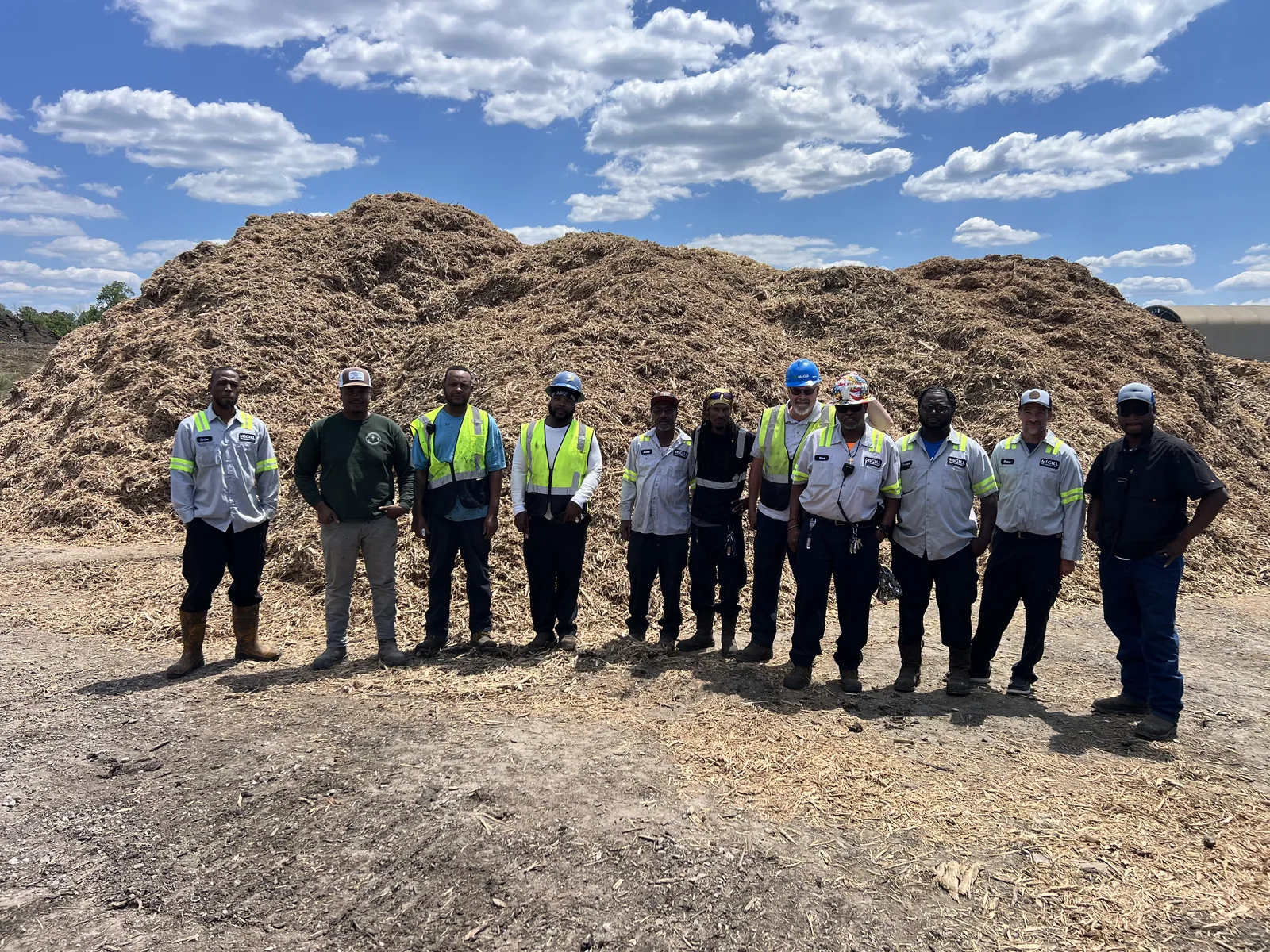 McGill plant team standing together in front of a large mulch pile on a sunny day